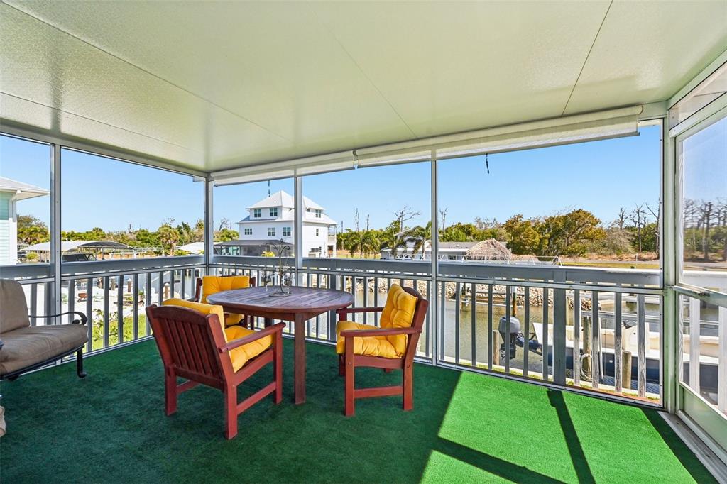 A screened-in porch features a wooden dining set, green carpeting, and views of the water — 10467 SHERMAN STREET, ENGLEWOOD, FL