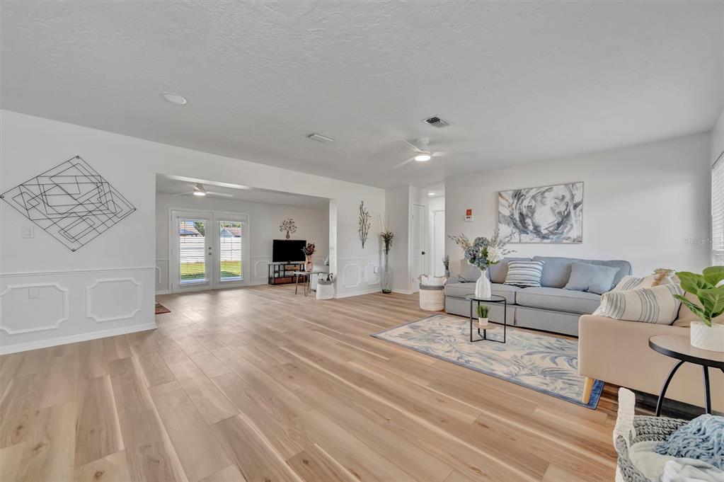 A bright living room features light wood-look flooring, a gray sofa, and white wainscoting — 6209 FLAMINGO DRIVE, APOLLO BEACH, FL