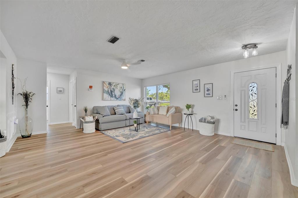 A living room features light wood-look flooring, white walls, a gray sofa, and a front door — 6209 FLAMINGO DRIVE, APOLLO BEACH, FL