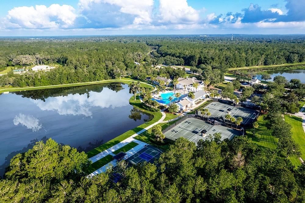An aerial view shows a lake, a swimming pool, and several tennis courts near buildings — 19987 ENGLISH WALNUT PLACE, BROOKSVILLE, FL