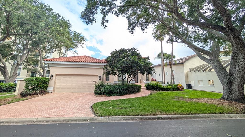 A tan house with a red tile roof and a brick driveway sits under large trees — 4709 DOLPHIN CAY LANE, ST PETERSBURG, FL