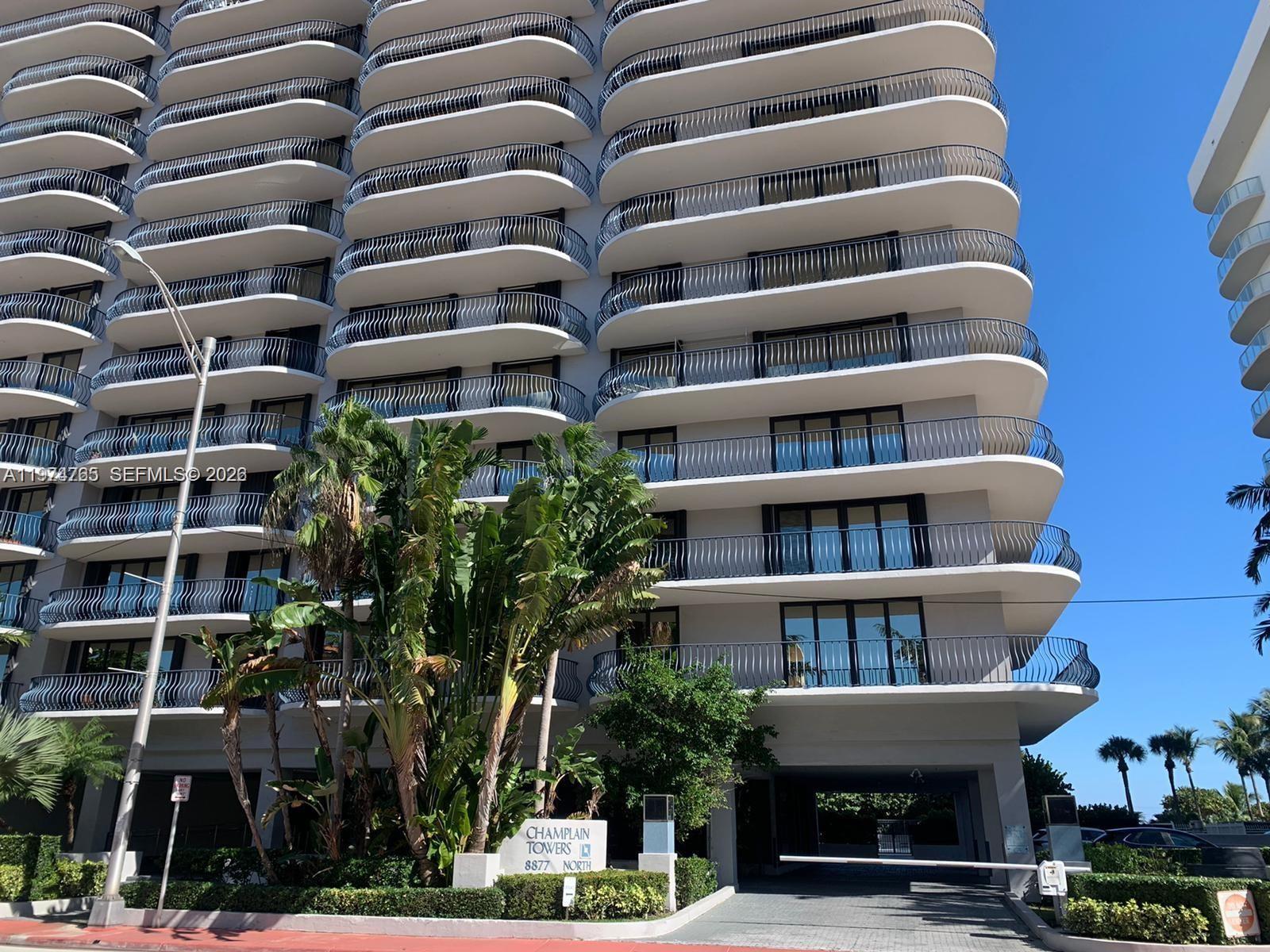 A multi-story residential building features curved balconies with dark railings and a ground-level gated entrance — 8877 Collins Avenue # 506, Surfside FL 33154, SURFSIDE, FL