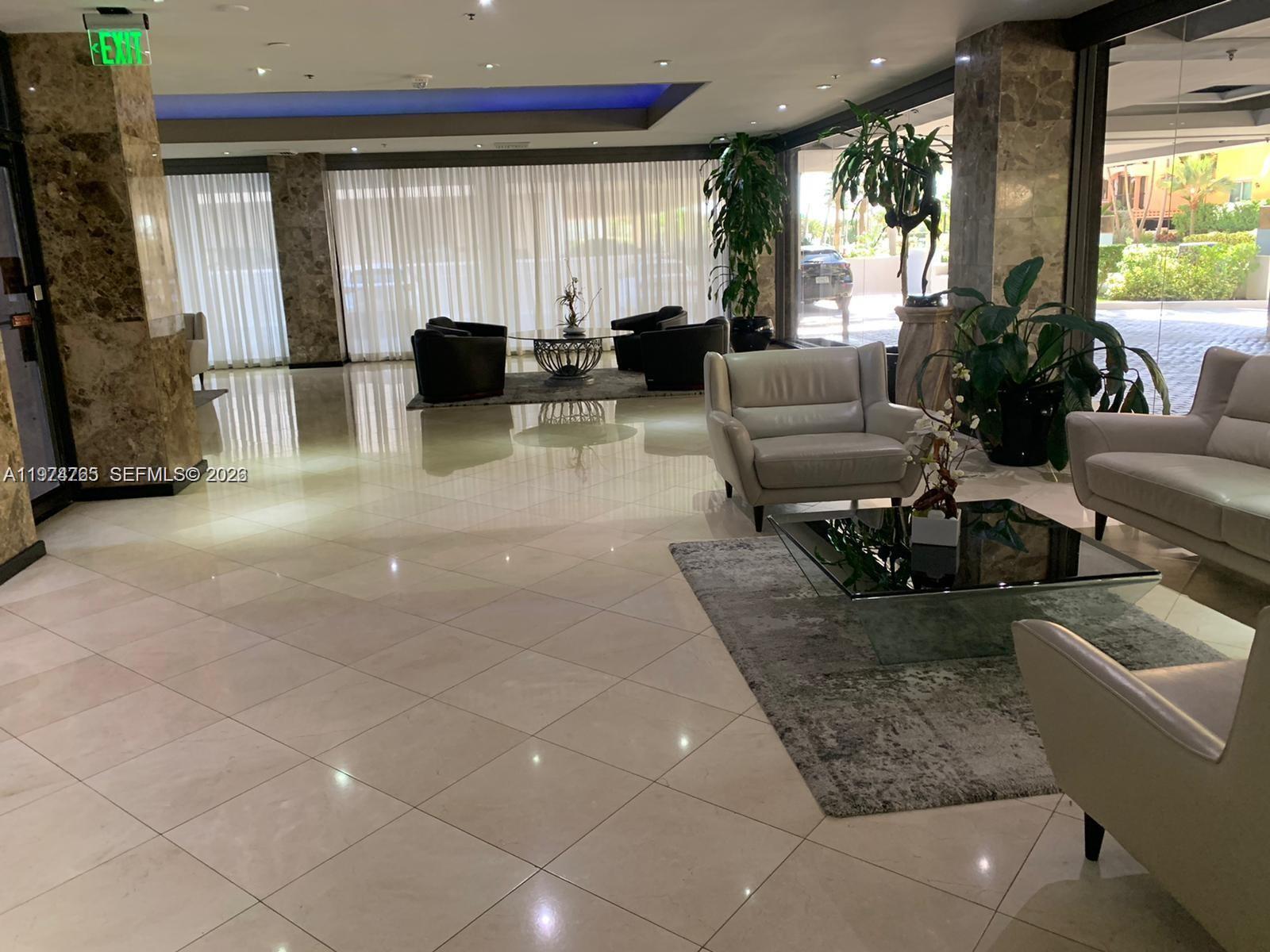 A modern lobby features marble floors, floor-to-ceiling windows with sheer curtains, and leather seating areas — 8877 Collins Avenue # 506, Surfside FL 33154, SURFSIDE, FL