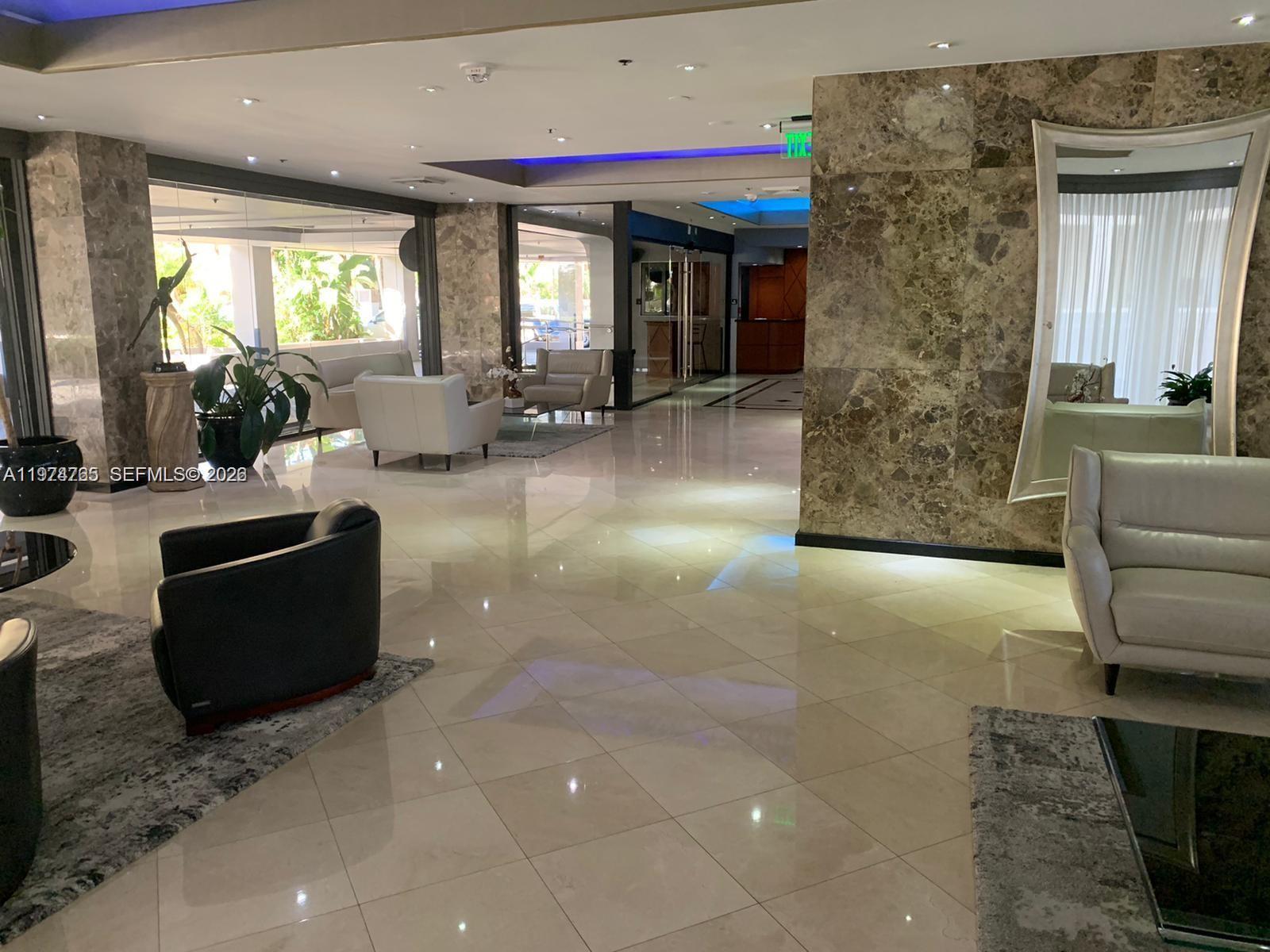 A modern building lobby features marble floors, neutral-toned seating, and a large wall mirror — 8877 Collins Avenue # 506, Surfside FL 33154, SURFSIDE, FL