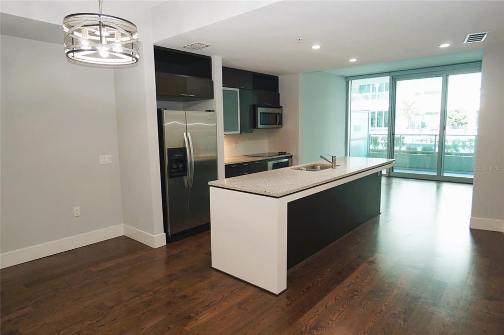 A modern kitchen features a granite-topped island, stainless steel appliances, and dark wood flooring — 111 N 12TH STREET UNIT 1320, TAMPA, FL