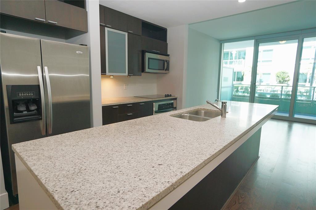 A modern kitchen features dark cabinetry, stainless steel appliances, and a large granite-topped island — 111 N 12TH STREET UNIT 1320, TAMPA, FL