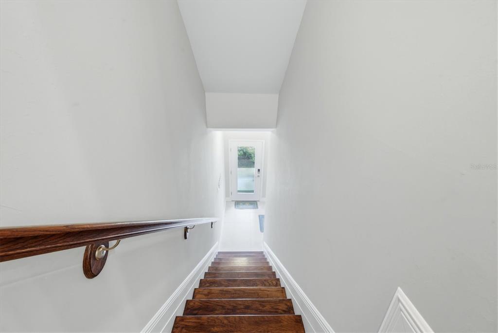 A wooden staircase with a handrail leads down toward a white exterior door — 10425 PILOTHOUSE COURT UNIT 131, PLACIDA, FL