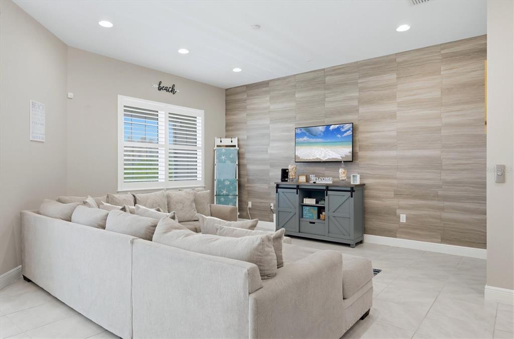 A living room features a large sectional sofa, a television, and a wood-paneled accent wall — 10425 PILOTHOUSE COURT UNIT 131, PLACIDA, FL