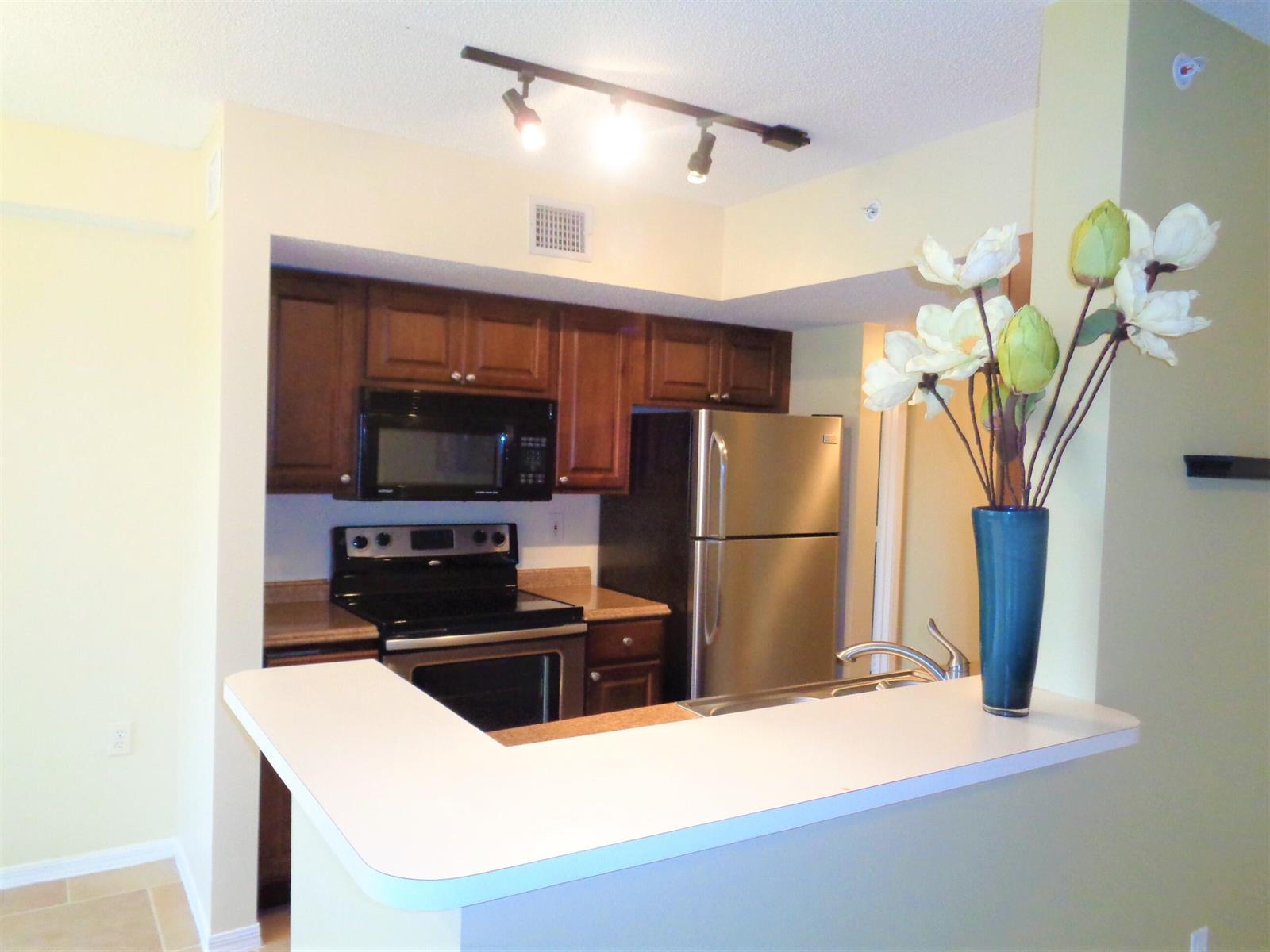 A kitchen features dark wood cabinets, stainless steel appliances, and a white breakfast bar counter — 1650 N 42nd Circle # 206, Vero Beach FL 32967, VERO BEACH, FL