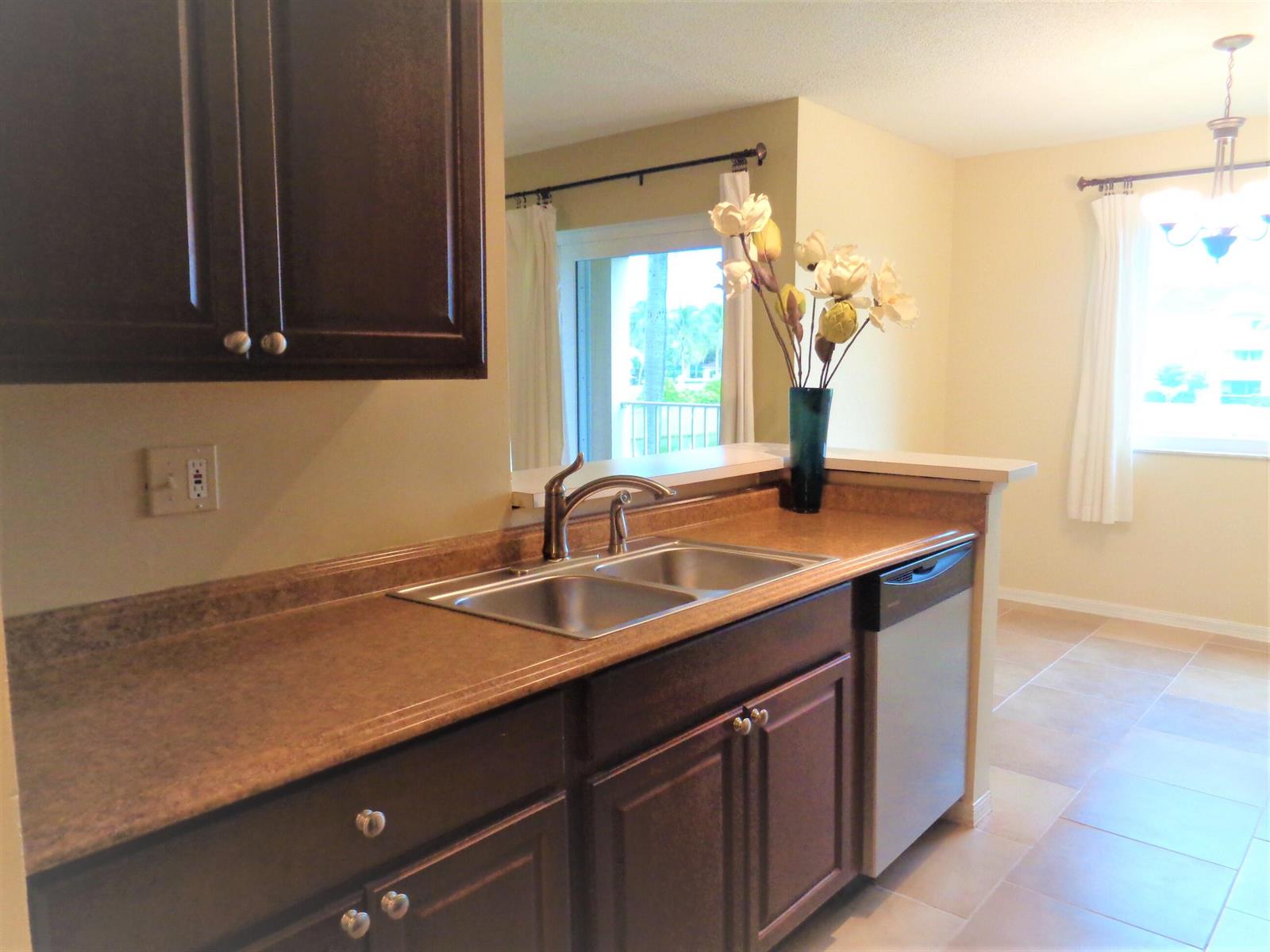 A kitchen features dark wood cabinets, a stainless steel sink, and a dishwasher — 1650 N 42nd Circle # 206, Vero Beach FL 32967, VERO BEACH, FL
