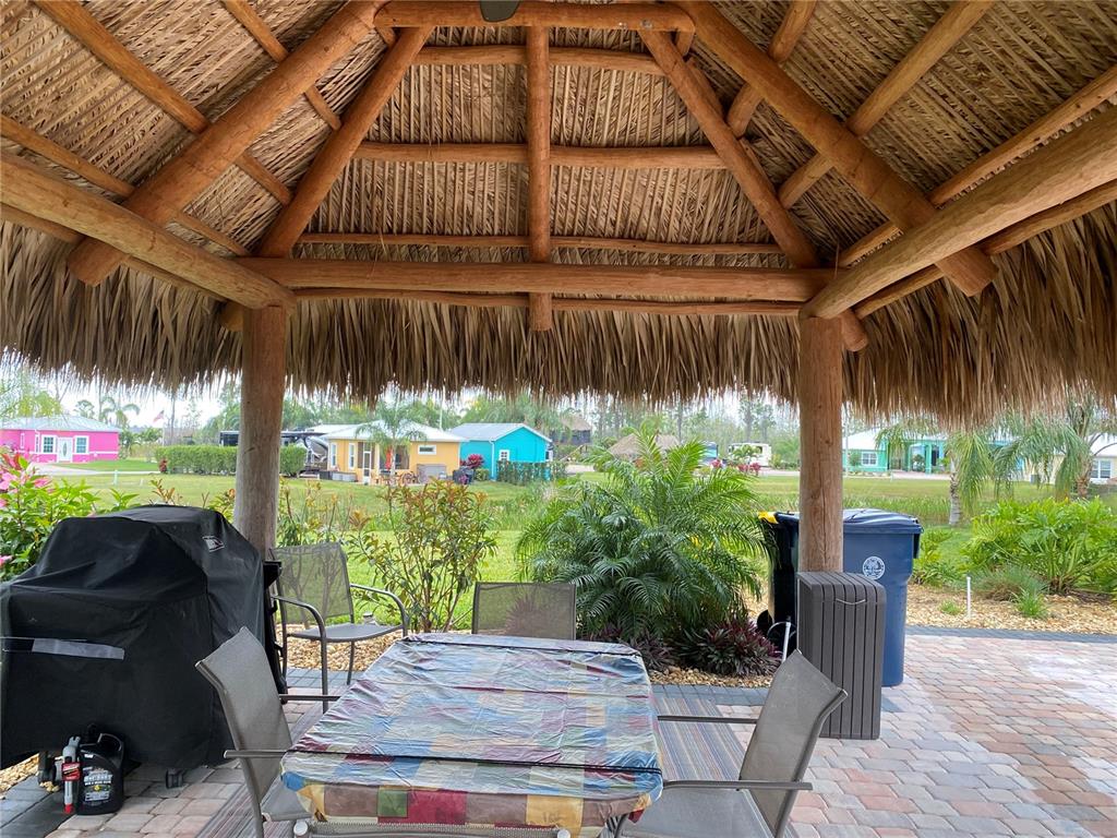 A covered outdoor patio with a thatched roof features a dining table and a grill — 3258 RED TAIL HAWK DRIVE, POLK CITY, FL