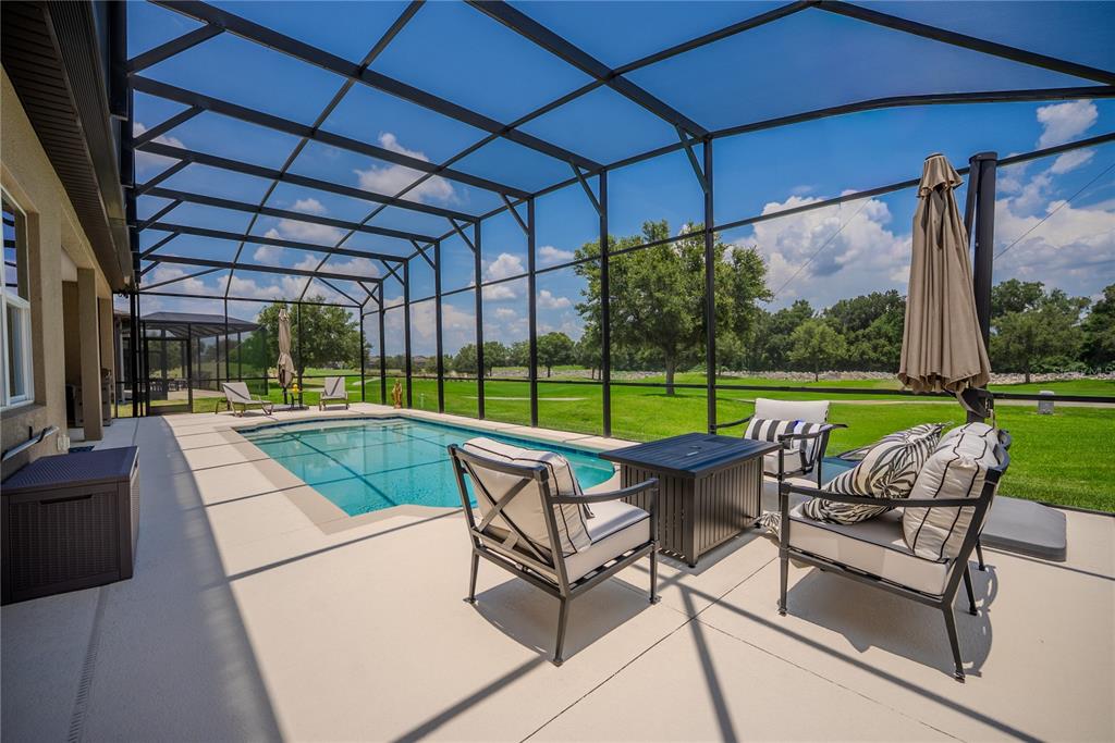 A screened-in patio features a swimming pool, outdoor seating, and a view of a golf course — 9125 SW 57TH PLACE ROAD, OCALA, FL