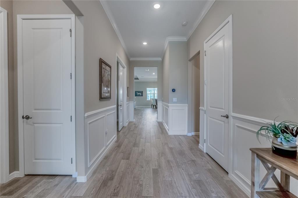 A hallway with light wood flooring, white wainscoting, and white doors leads to a bright room — 9125 SW 57TH PLACE ROAD, OCALA, FL