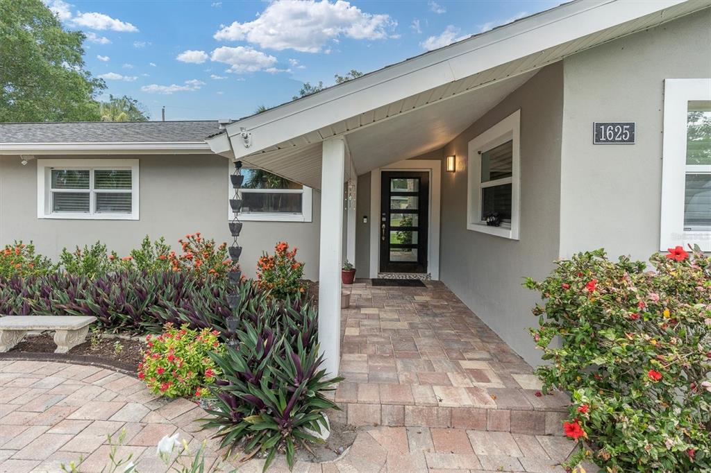 A paved walkway leads to the front entrance of a house with gray siding — 1625 NORTH DAKOTA AVENUE NE, ST PETERSBURG, FL