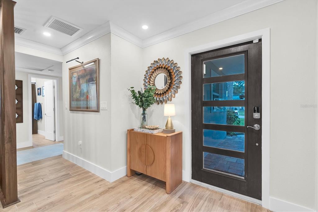 An entryway features a wooden console table, a sunburst mirror, and a dark glass-paneled door — 1625 NORTH DAKOTA AVENUE NE, ST PETERSBURG, FL
