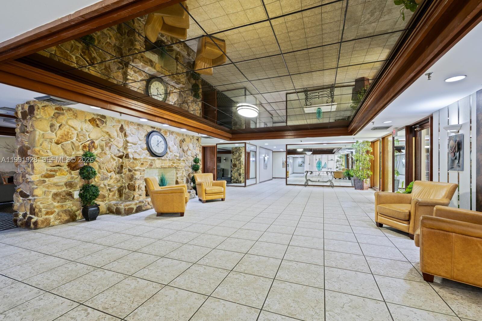 A spacious lobby features a stone fireplace, tan leather armchairs, and a mirrored grid ceiling — 665 NE 195th St # 222, Miami FL 33179, MIAMI, FL
