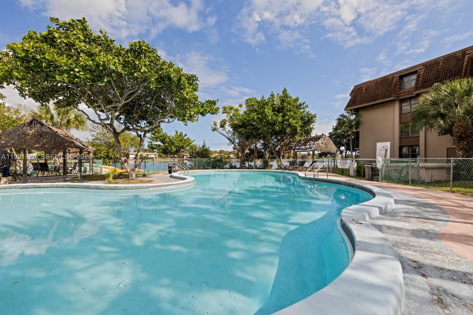 A swimming pool with a tiki hut sits outside a multi-story apartment building — 665 NE 195th St # 222, Miami FL 33179, MIAMI, FL
