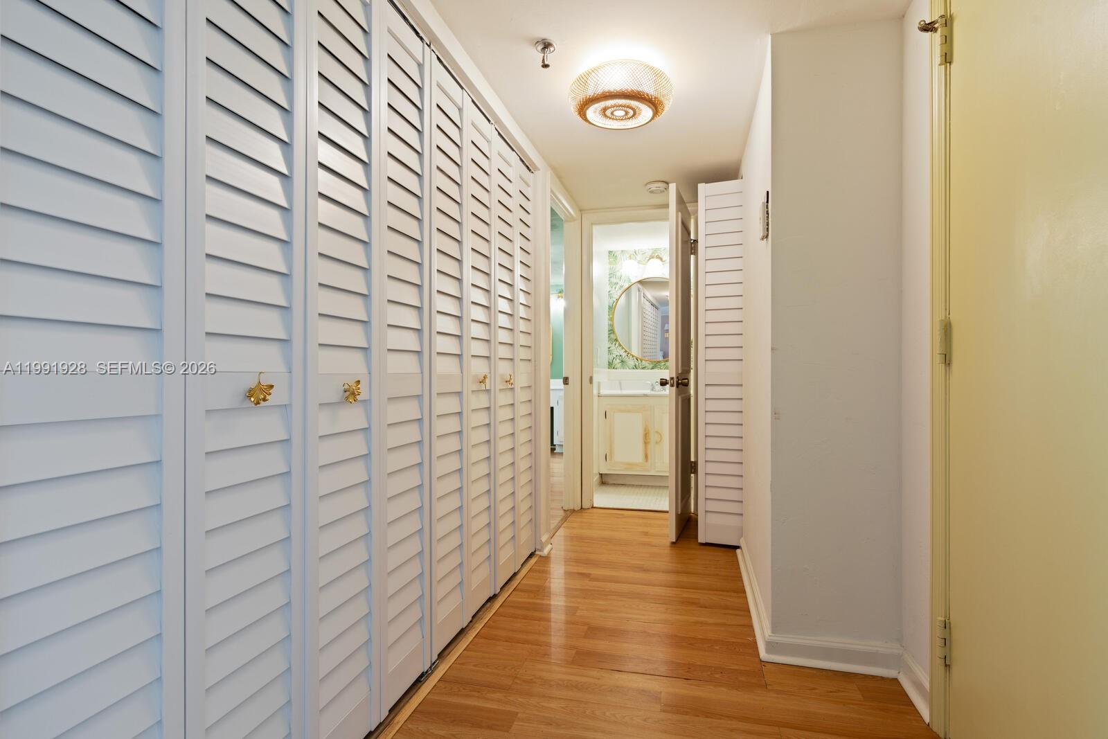 A hallway features light wood flooring, louvered closet doors, and a view into a bathroom — 665 NE 195th St # 222, Miami FL 33179, MIAMI, FL