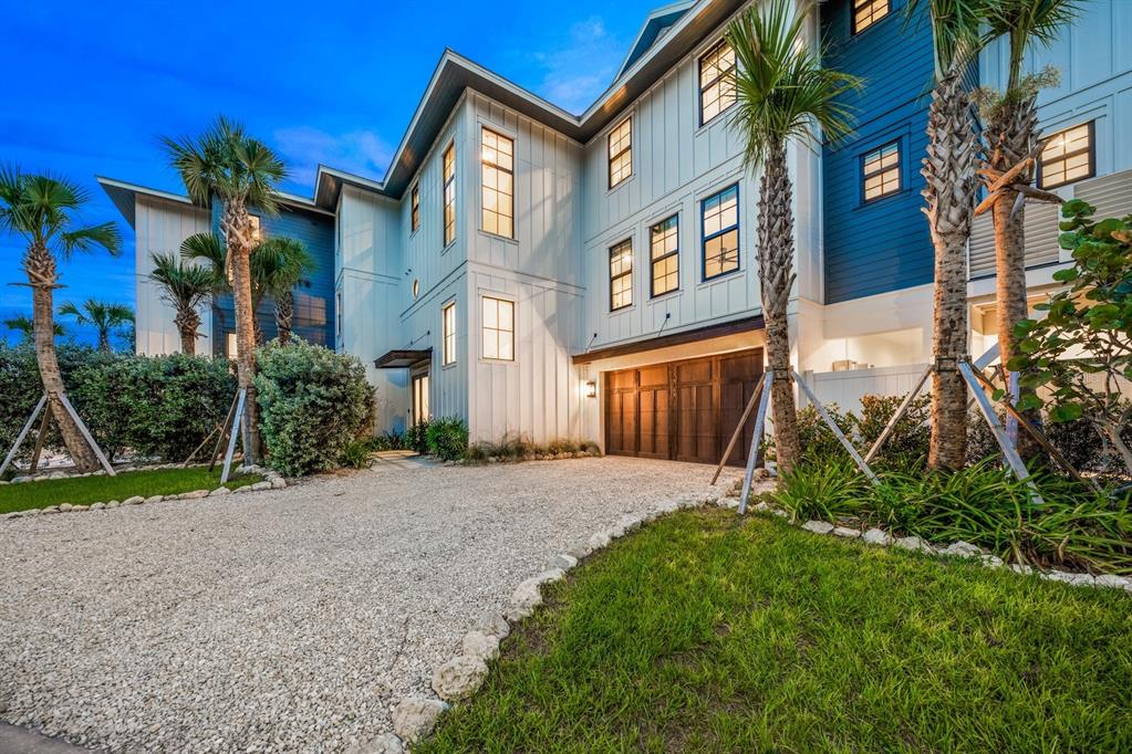 A multi-story house with white vertical siding, blue accents, and a gravel driveway at dusk — 6910 MIDNIGHT PASS ROAD UNIT A, SARASOTA, FL