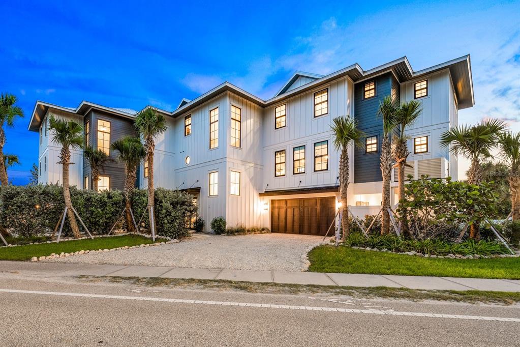A three-story coastal home with white siding, dark accents, and a gravel driveway at dusk — 6910 MIDNIGHT PASS ROAD UNIT A, SARASOTA, FL