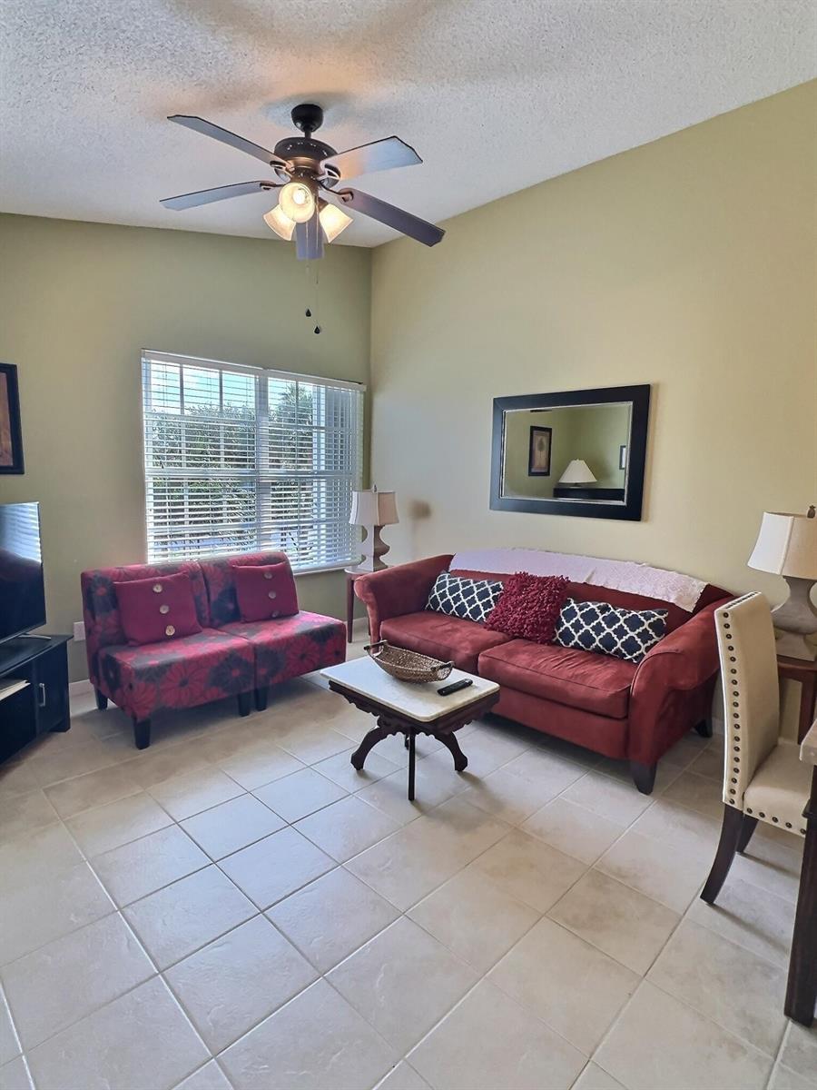 A living room features a red sofa, a patterned loveseat, and tile flooring — 117 Waterside Drive # 117, Hypoluxo FL 33462, HYPOLUXO, FL