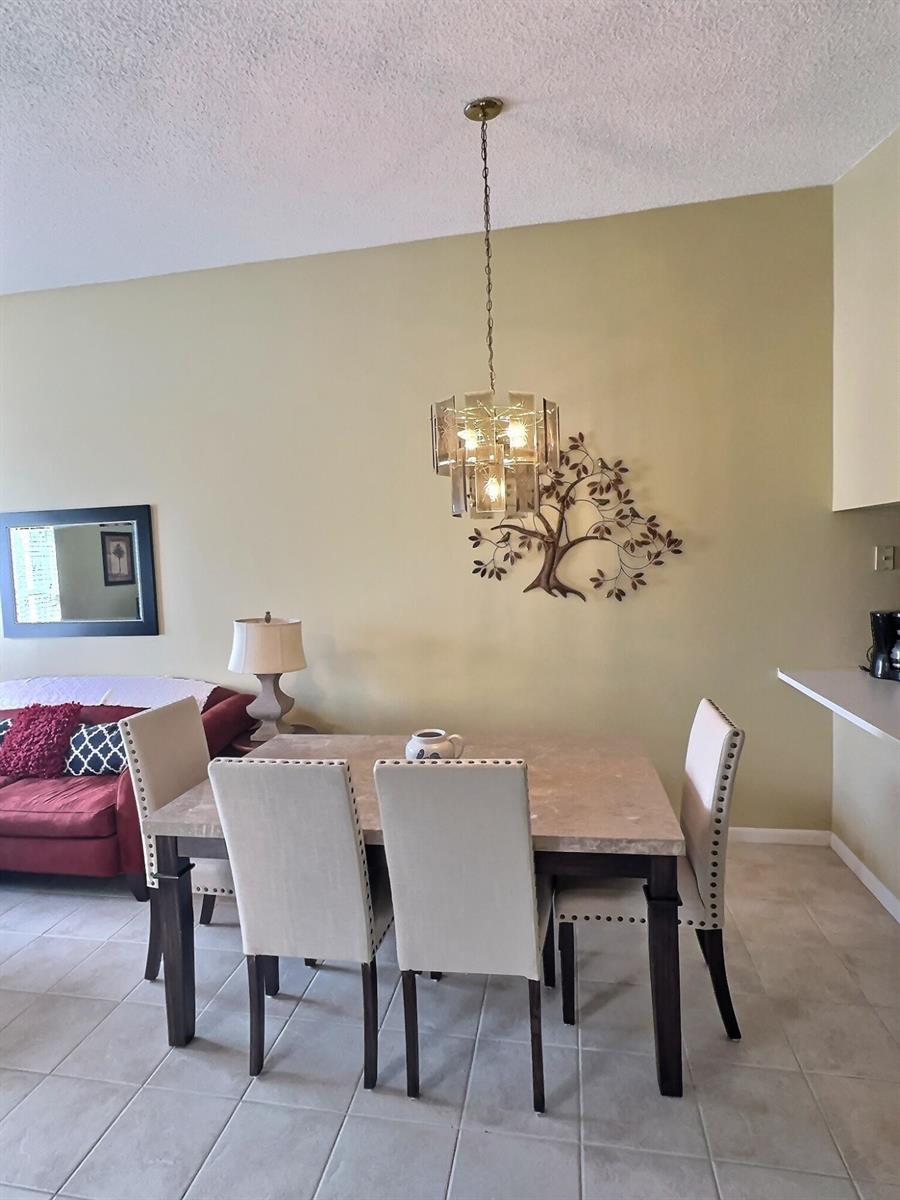 A dining area features a stone-topped table, four upholstered chairs, and a metal tree wall sculpture — 117 Waterside Drive # 117, Hypoluxo FL 33462, HYPOLUXO, FL