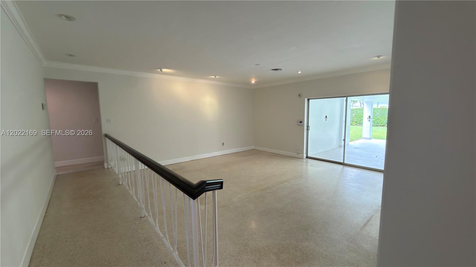 An empty room features beige carpet, a dark wood handrail, and sliding glass doors — 7700 SW 52nd Ct, Miami FL 33143, MIAMI, FL