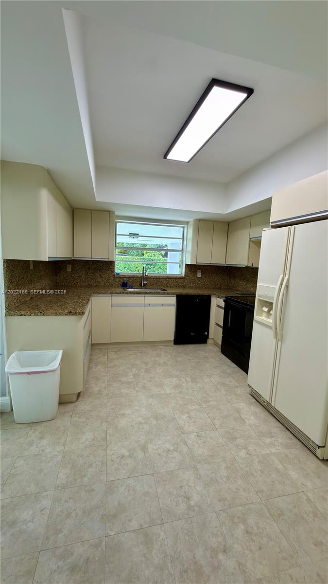 A kitchen features beige cabinets, granite countertops, black appliances, and light-colored tile flooring — 7700 SW 52nd Ct, Miami FL 33143, MIAMI, FL