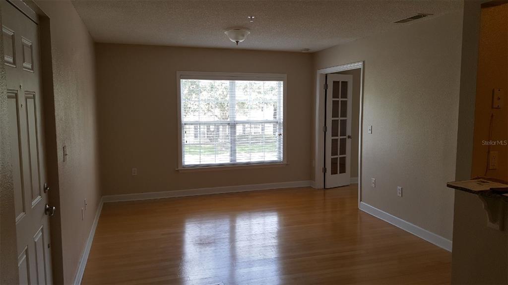 An empty room features light-colored hardwood floors, beige walls, a central window, and a door — 2035 DIXIE BELLE DRIVE UNIT 2035O, ORLANDO, FL