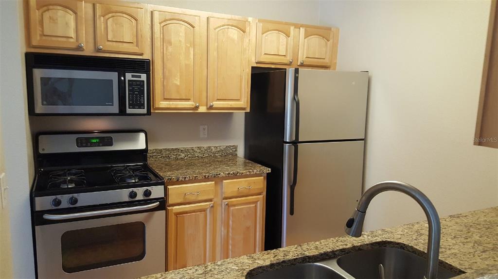 A kitchen features light wood cabinets, granite countertops, and stainless steel appliances — 2035 DIXIE BELLE DRIVE UNIT 2035O, ORLANDO, FL