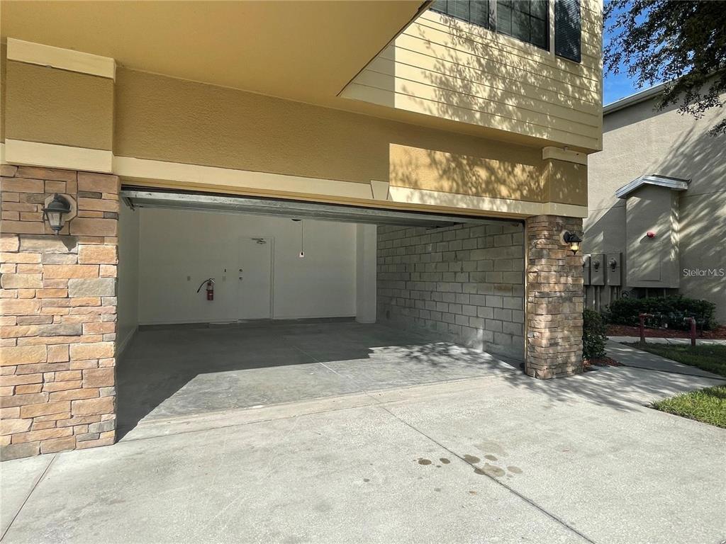 An open garage with concrete flooring, stone pillars, and a white door at the back — 3408 SENECA CLUB LOOP UNIT C, ORLANDO, FL
