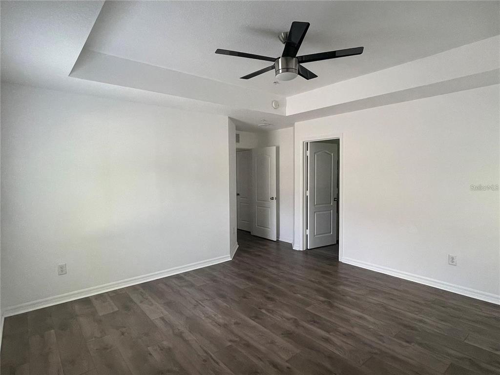 A bedroom features white walls, a tray ceiling with a fan, and wood-look flooring — 3408 SENECA CLUB LOOP UNIT C, ORLANDO, FL