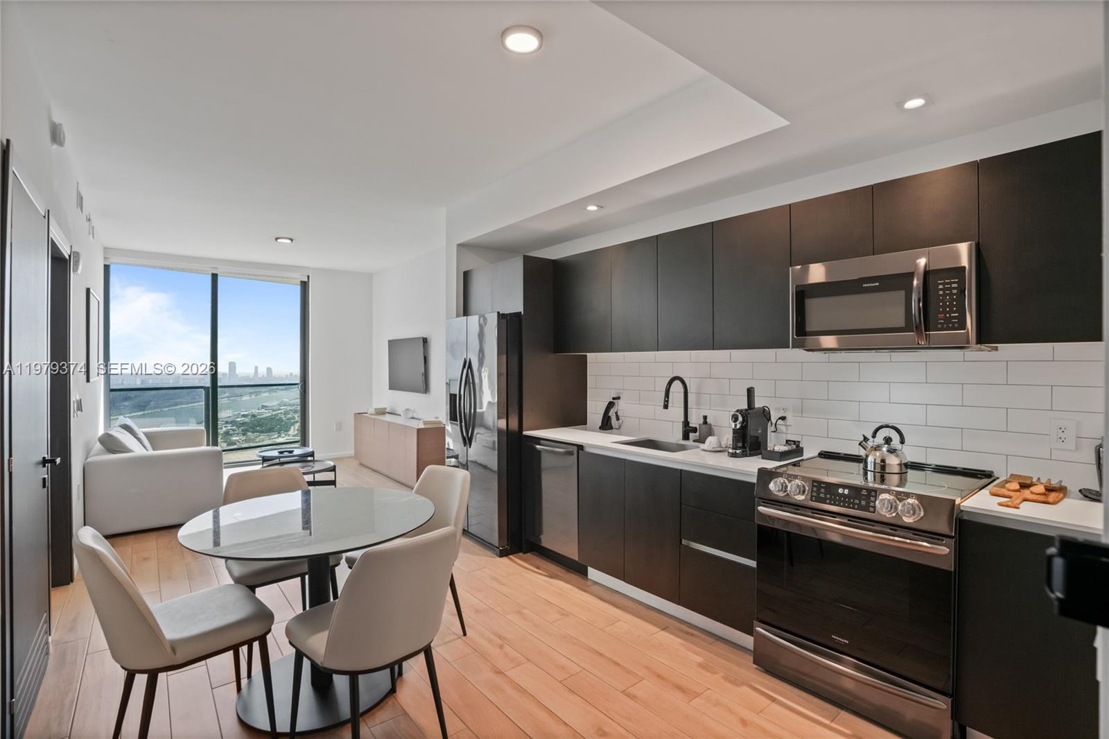 A modern kitchen and dining area with dark cabinetry, stainless appliances, and floor-to-ceiling windows — 398 NE 5th St # 4410, Miami FL 33132, MIAMI, FL