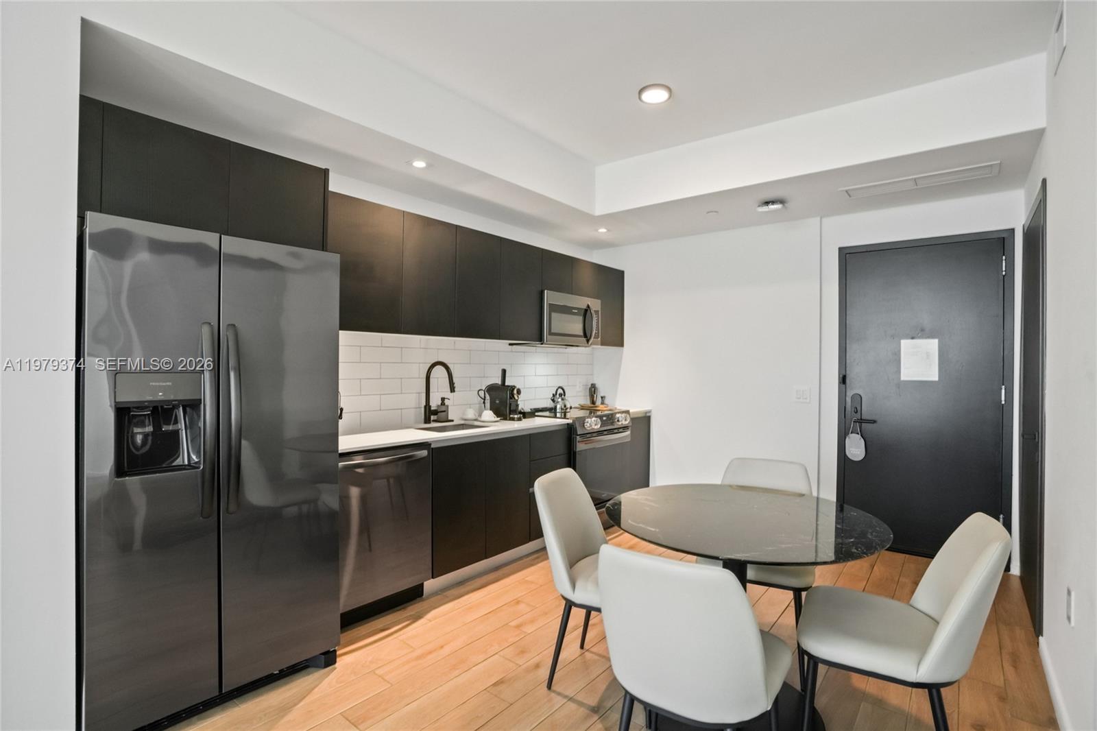 A modern kitchen features dark cabinetry, stainless steel appliances, and a round dining table — 398 NE 5th St # 4410, Miami FL 33132, MIAMI, FL