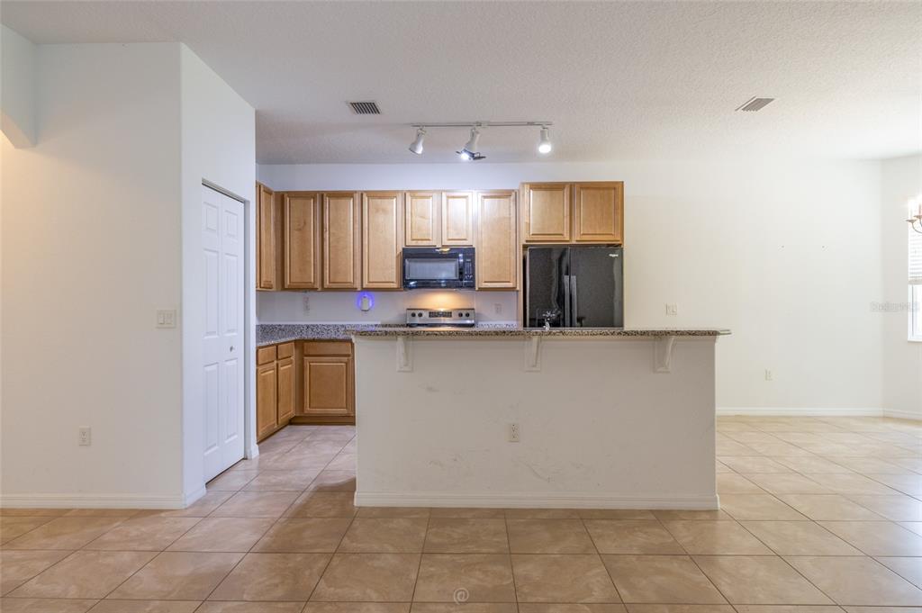 A kitchen features light wood cabinets, granite countertops, a black refrigerator, and tile flooring — 95 BICKFORD DRIVE, PALM COAST, FL
