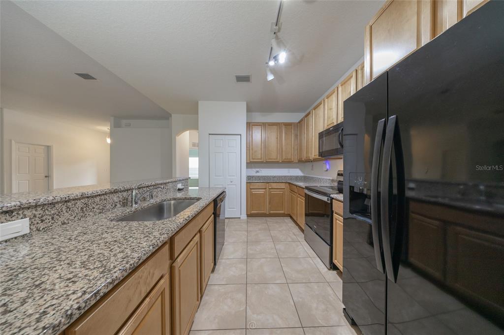 A kitchen features light wood cabinets, granite countertops, tile flooring, and black appliances — 95 BICKFORD DRIVE, PALM COAST, FL