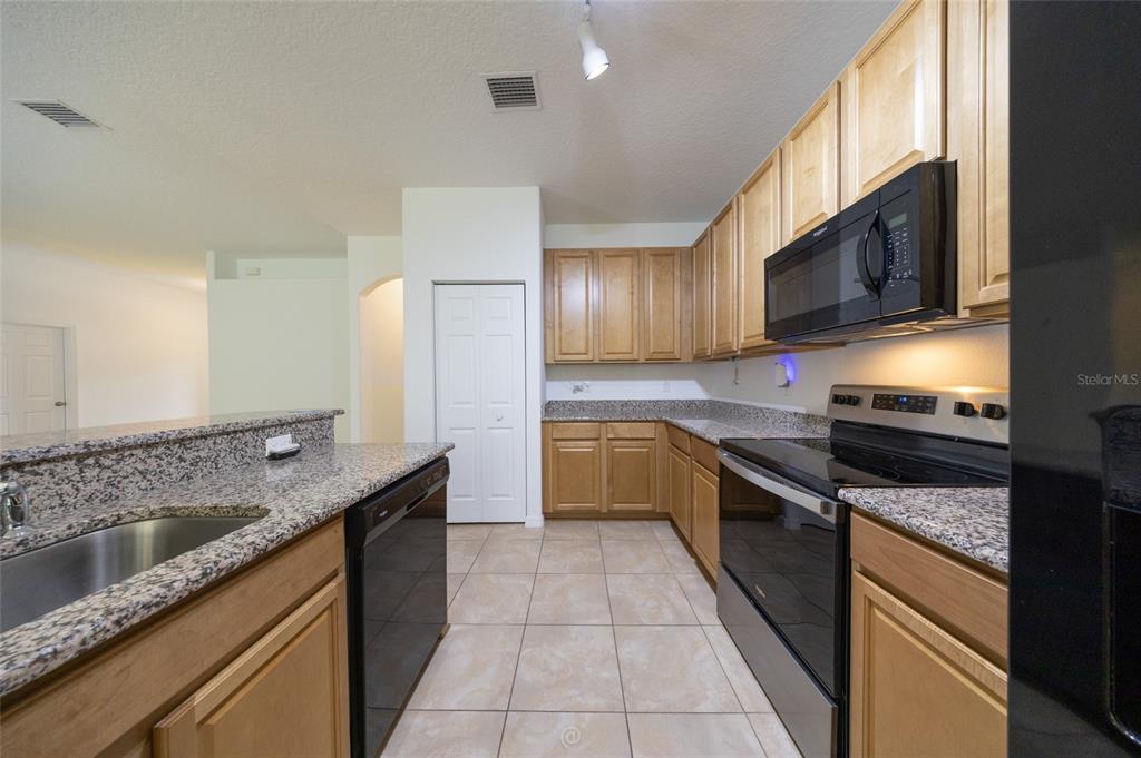 A kitchen features light wood cabinets, granite countertops, black appliances, and beige tile flooring — 95 BICKFORD DRIVE, PALM COAST, FL