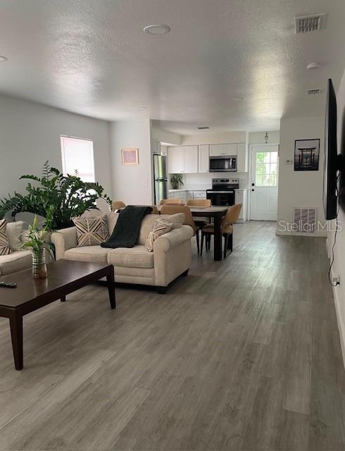 An open-concept living room features light wood-look flooring, a beige sofa, and a kitchen beyond — 120 B STREET, LAKE WALES, FL