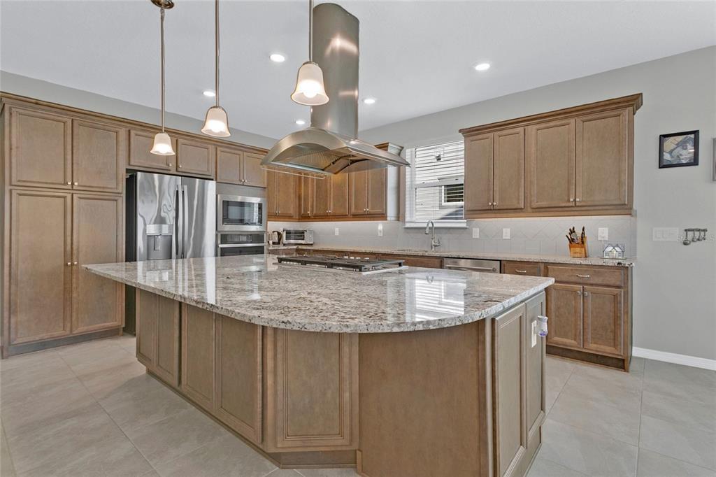 A kitchen features a large granite-topped island, stainless steel appliances, and wood cabinetry — 4339 NW 56TH COURT, OCALA, FL