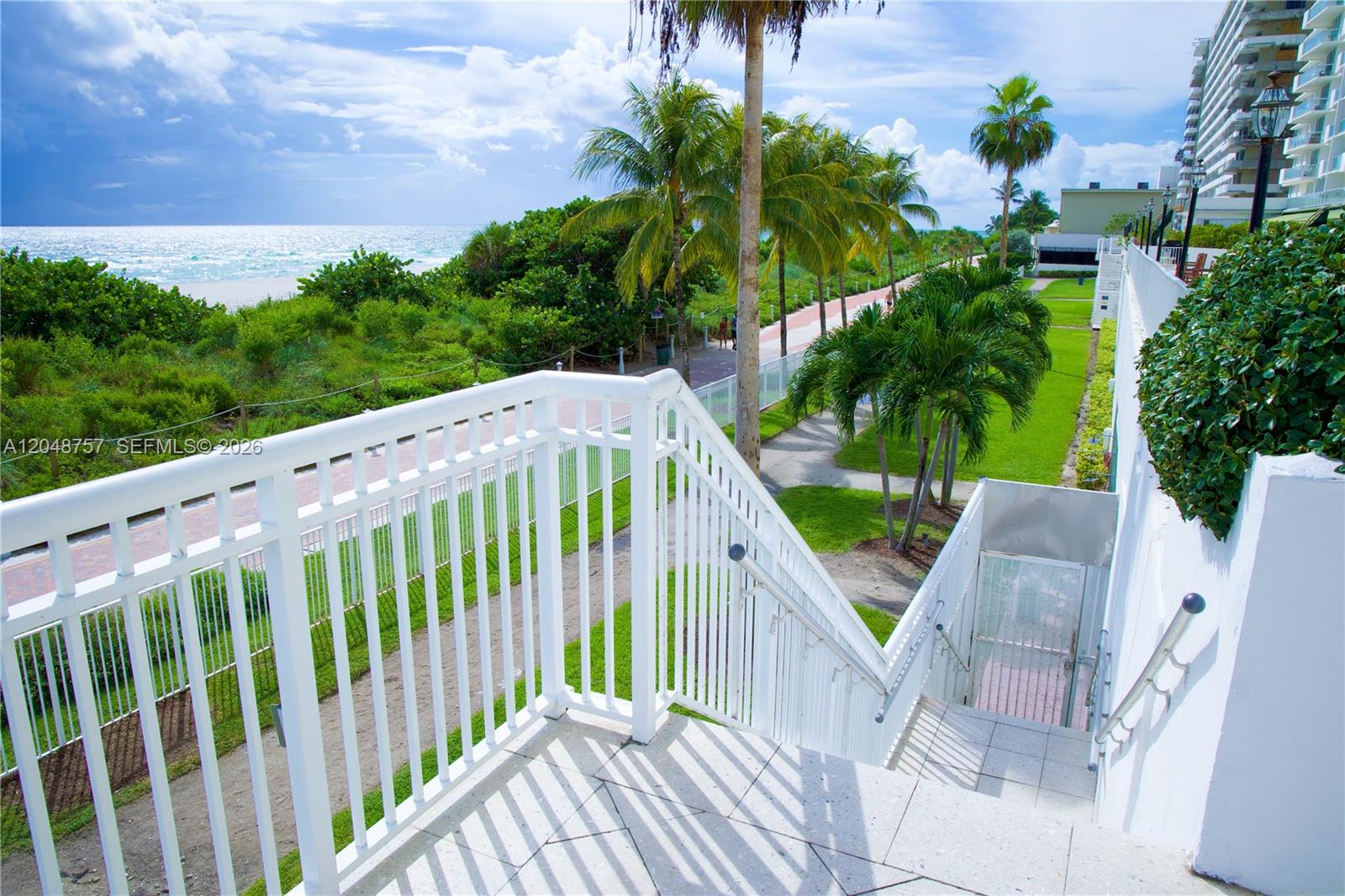 An outdoor staircase with white railings overlooks a beach path, palm trees, and the ocean — 5601 Collins Ave # 1614, Miami Beach FL 33140, MIAMI BEACH, FL