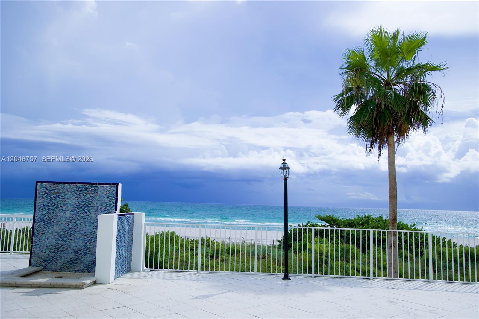 A tiled patio overlooks a beach with a palm tree, a shower, and a lamp post — 5601 Collins Ave # 1614, Miami Beach FL 33140, MIAMI BEACH, FL