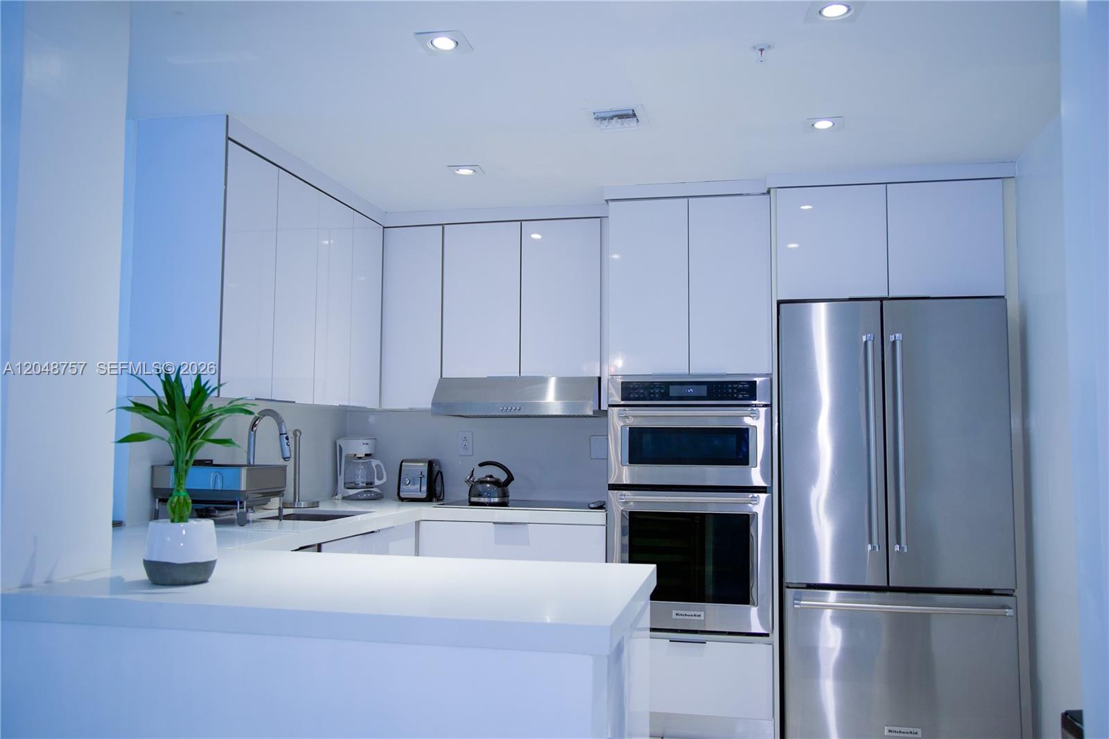 A modern kitchen features white glossy cabinets, stainless steel appliances, and a white countertop — 5601 Collins Ave # 1614, Miami Beach FL 33140, MIAMI BEACH, FL