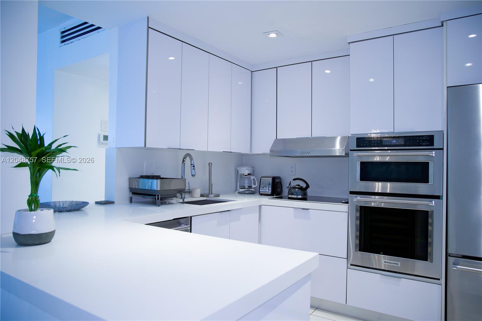 A modern kitchen features white glossy cabinets, stainless steel appliances, and a white countertop — 5601 Collins Ave # 1614, Miami Beach FL 33140, MIAMI BEACH, FL