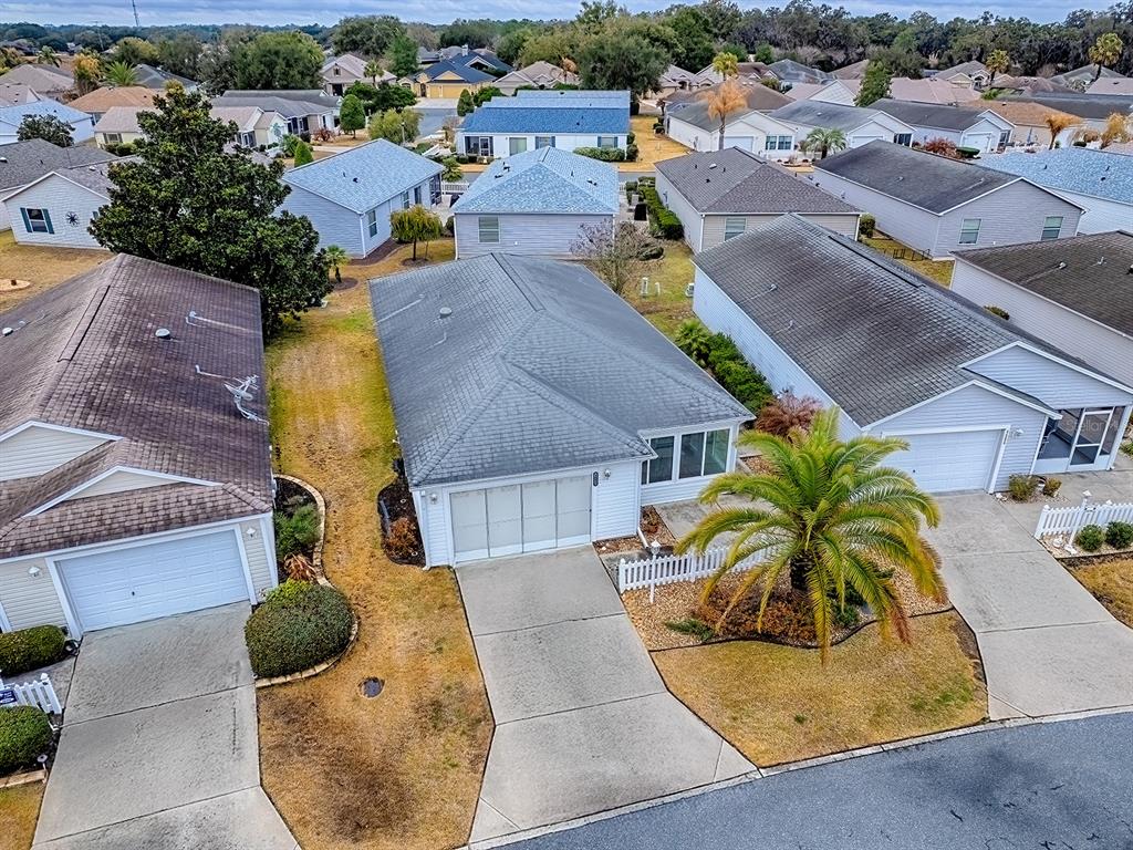 A concrete patio sits between two white-sided houses with a central air conditioning unit — 1692 INDIGO AVENUE, THE VILLAGES, FL