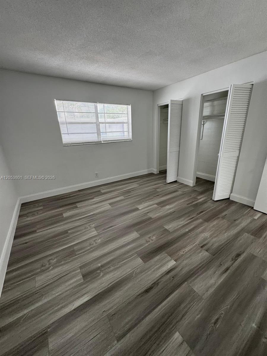 An empty bedroom features light gray walls, wood-look vinyl flooring, and two louvered closet doors — 2435 Van Buren St APT 2B, Hollywood FL 33020, HOLLYWOOD, FL