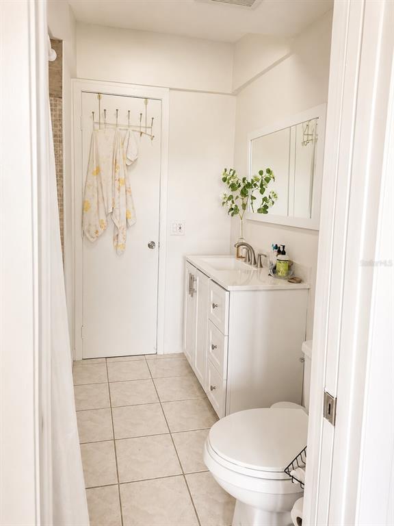 A bathroom features a white vanity, a toilet, a tiled floor, and a door with hooks — 2850 W GOLF BOULEVARD UNIT 212, POMPANO BEACH, FL