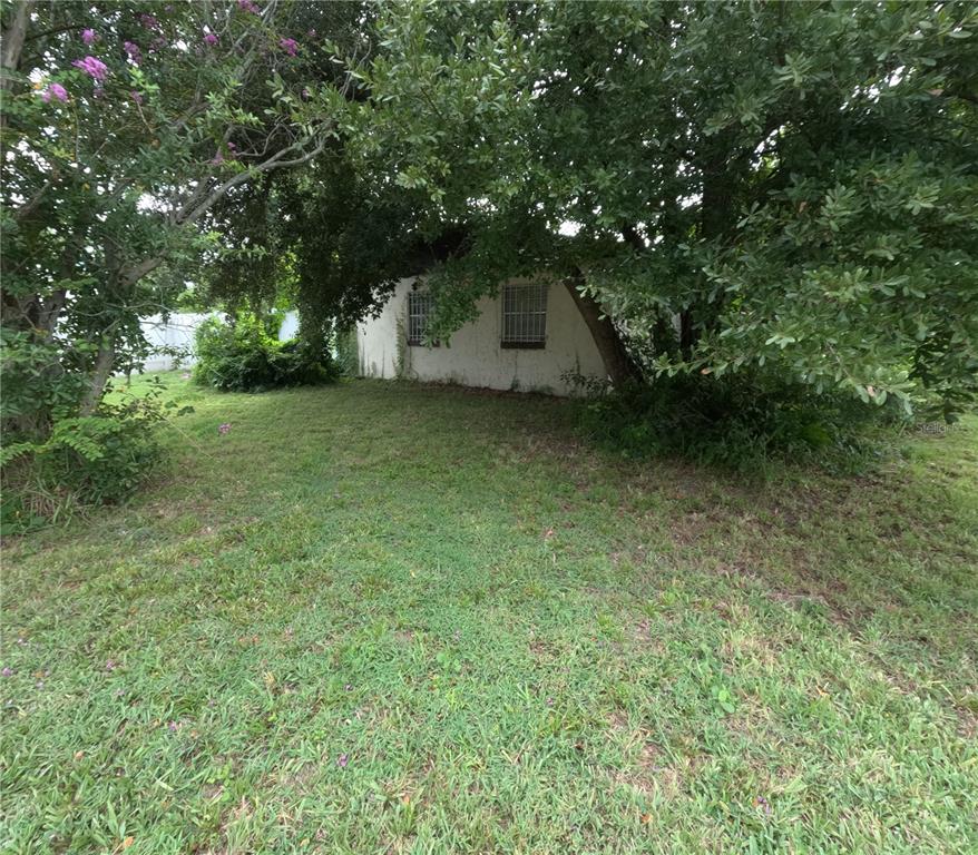 A small, white, single-story building is partially obscured by trees in a grassy yard — 3122 W SOUTH STREET, ORLANDO, FL