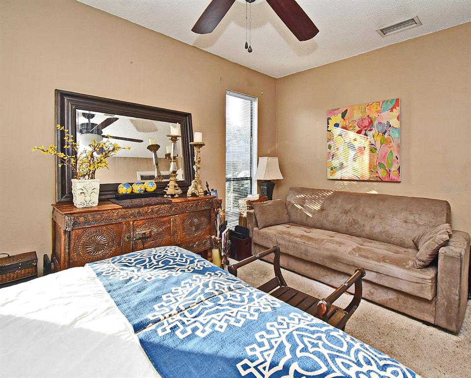 A bedroom features a bed with a blue patterned throw, a wooden dresser, and a sofa — 686 LAKE VILLAS DRIVE UNIT 686, ALTAMONTE SPRINGS, FL