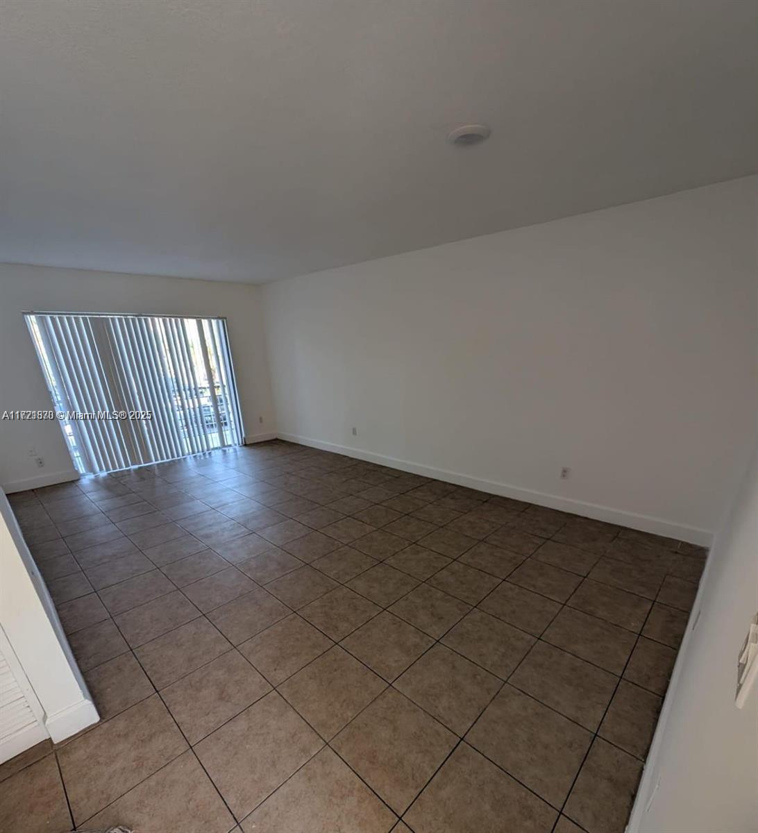 An empty room features white walls, tan tile flooring, and a sliding glass door with blinds — 2800 NW 56th Ave # B202, Lauderhill FL 33313, LAUDERHILL, FL