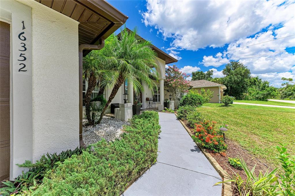 A black metal pergola covers a patio set in a grassy backyard with landscaping — 16352 CHICOPEE AVENUE, PORT CHARLOTTE, FL
